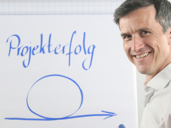 Mann leitet passgenaues Seminar und Training zur Führungskräfteentwicklung vor Flipchart mit der Beschriftung Projekterfolg