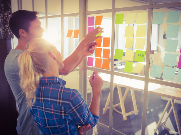 Zwei junge Menschen vor einer gläsernen Zettelwand
